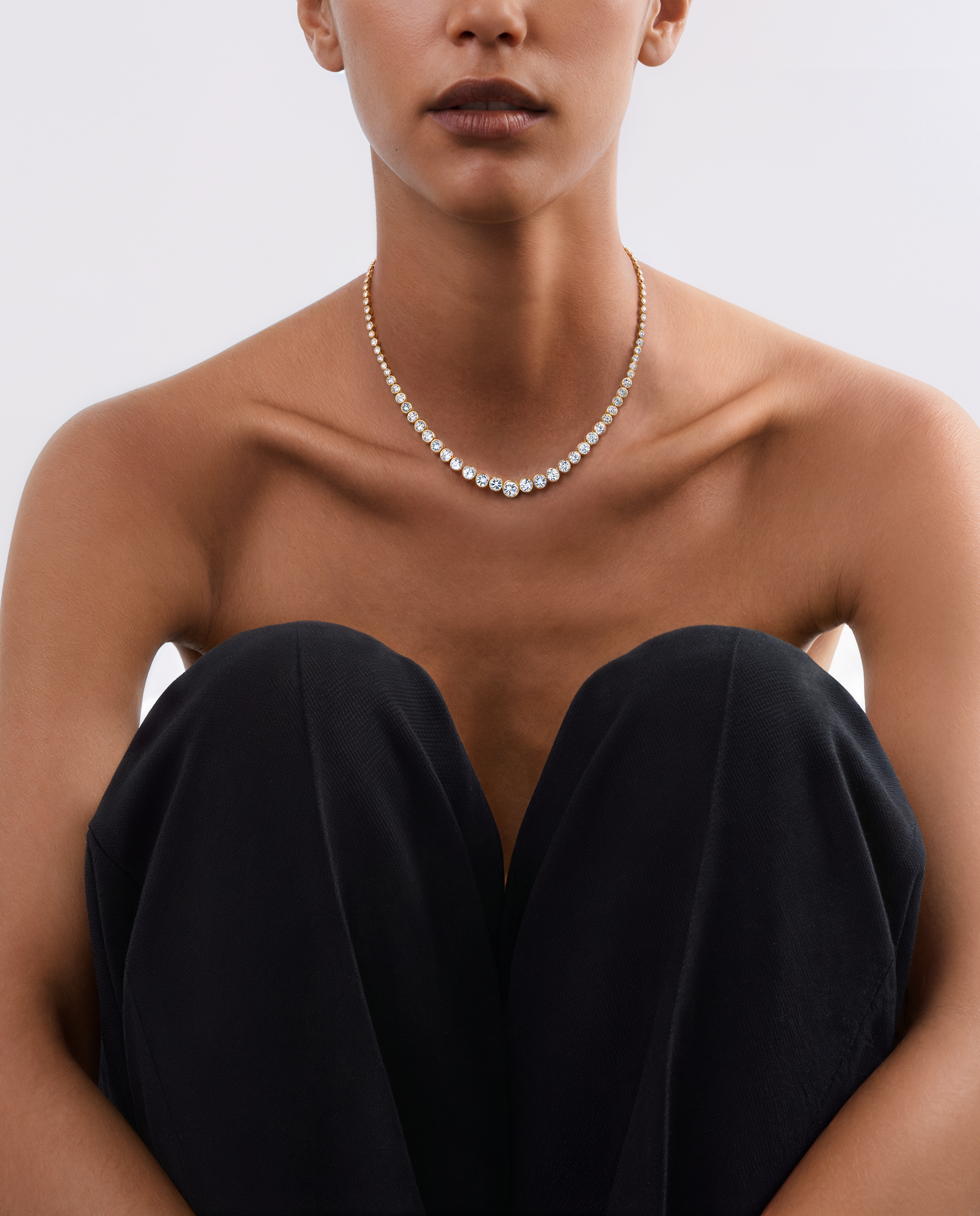 A close-up of a model wearing a delicate Harlow George Bezel set diamond tennis necklace in yellow gold.